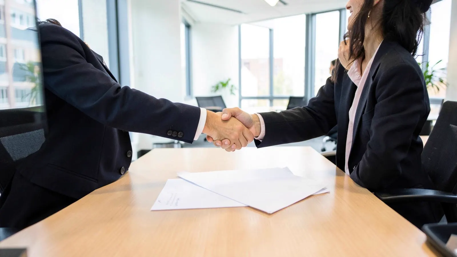 Two business people shaking hands over paperwork in a meeting room