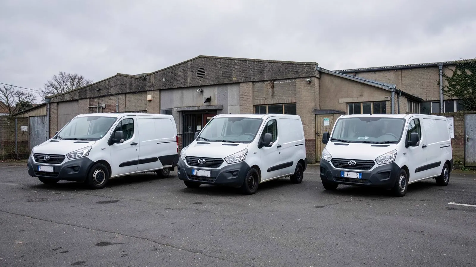 Row of plain white service vans parked outside a small British business unit